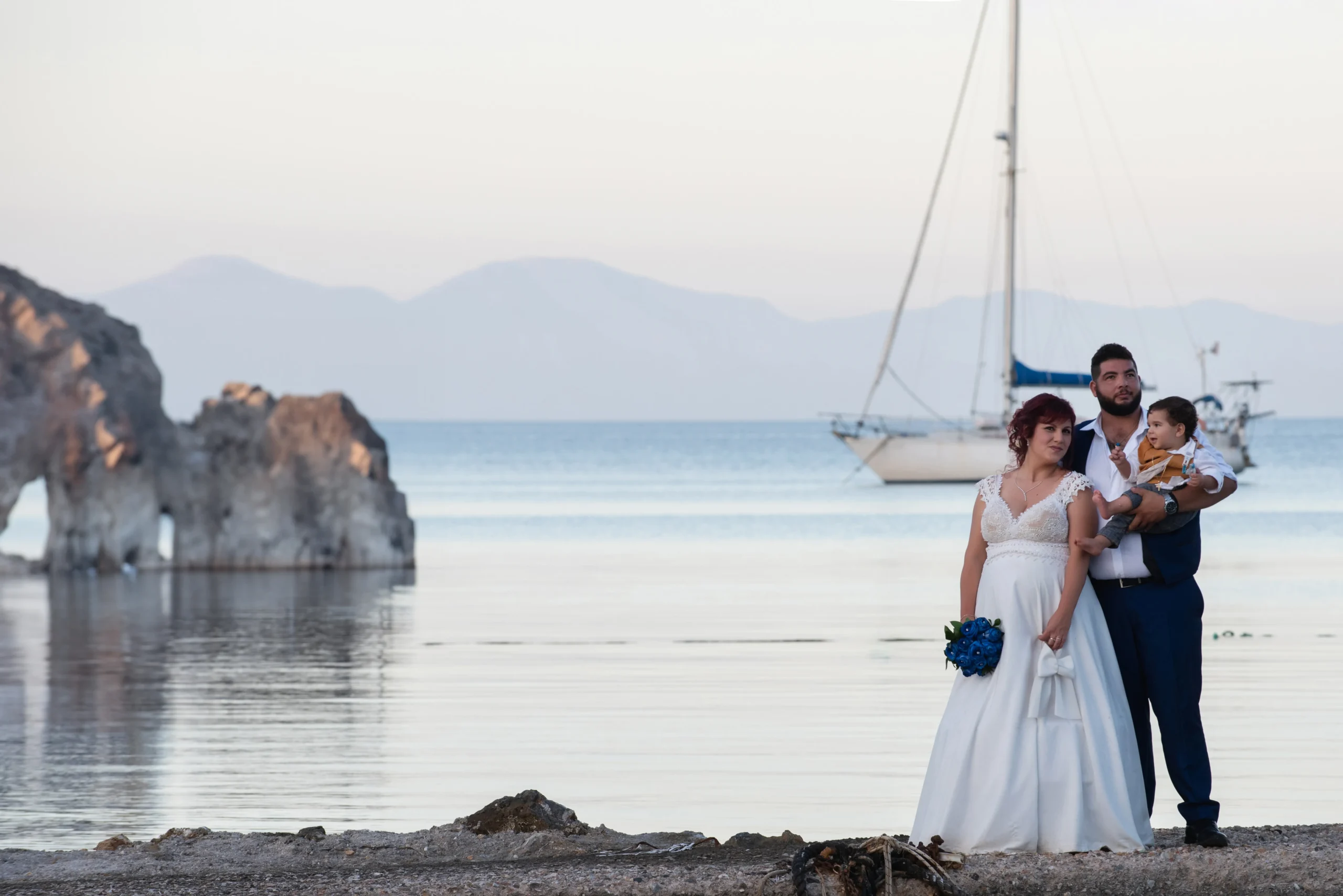 νύφη και γαμπρός με μωρό στην αγκαλιά με φόντο τη θάλασσα