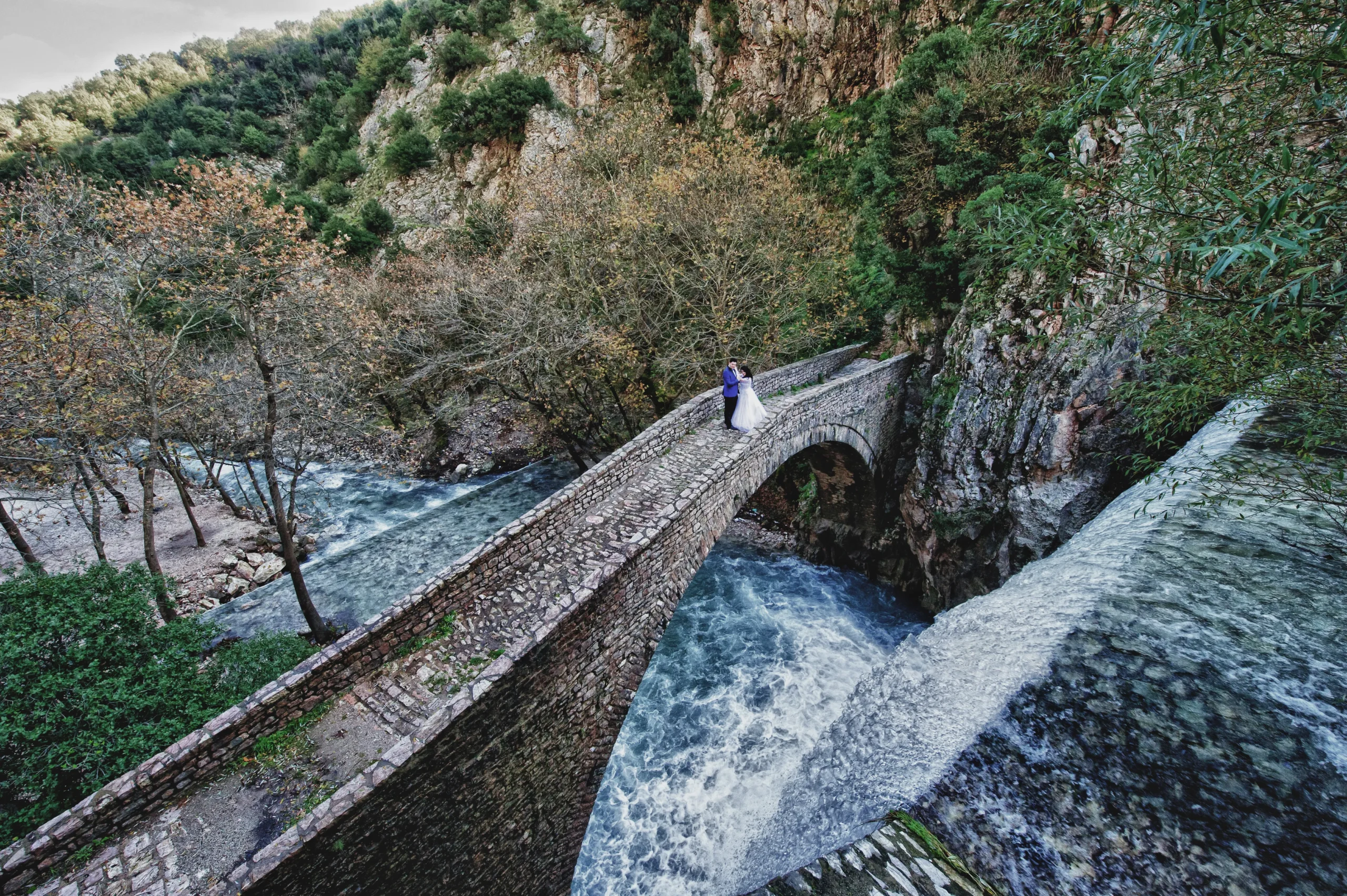 νύφη και γαμπρός πάνω σε πέτρινη γέφυρα